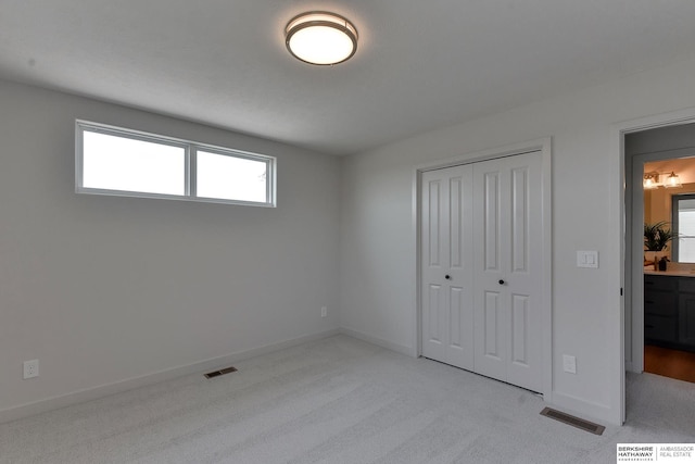 unfurnished bedroom featuring ensuite bath, light carpet, and a closet