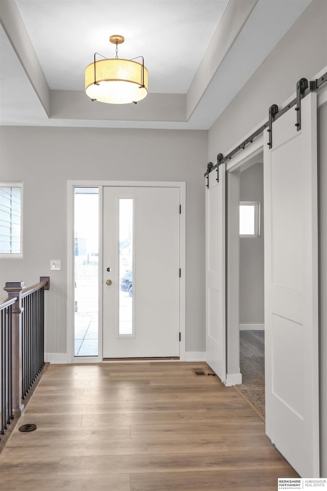 foyer entrance featuring hardwood / wood-style flooring, a barn door, and a raised ceiling