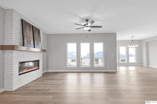 unfurnished living room featuring ceiling fan with notable chandelier, light wood-type flooring, and a brick fireplace