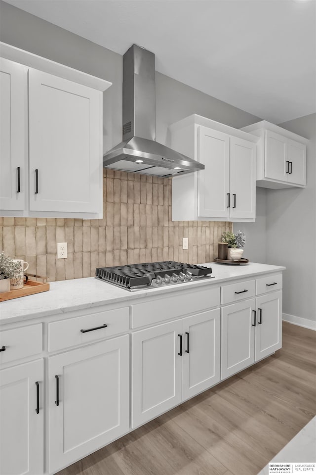 kitchen with decorative backsplash, white cabinets, and wall chimney range hood