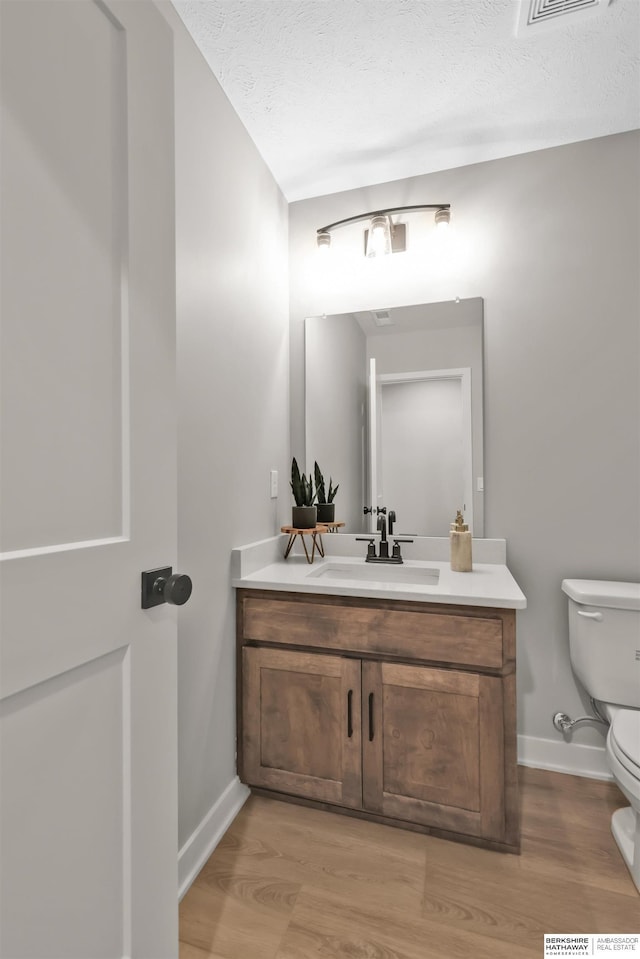 bathroom with vanity, toilet, wood-type flooring, and a textured ceiling