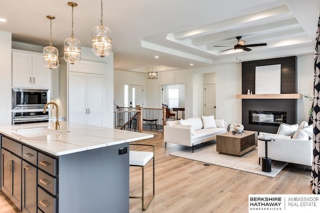 kitchen featuring stainless steel appliances, a raised ceiling, pendant lighting, a center island with sink, and white cabinetry