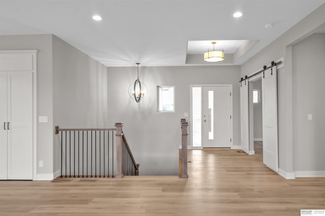 entryway featuring a barn door, light hardwood / wood-style flooring, a raised ceiling, and an inviting chandelier