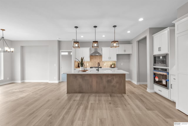 kitchen featuring built in microwave, white cabinetry, stainless steel oven, hanging light fixtures, and an island with sink