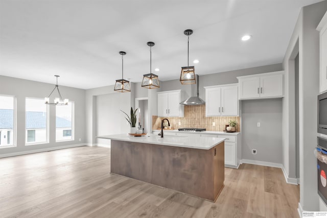 kitchen featuring white cabinetry, a center island with sink, and wall chimney exhaust hood