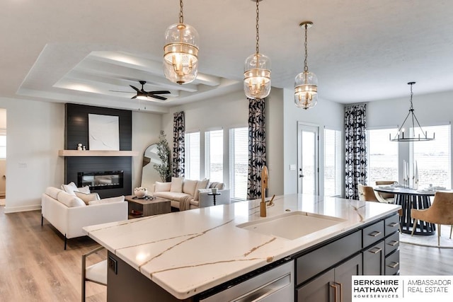 kitchen with a center island with sink, decorative light fixtures, light stone countertops, and sink