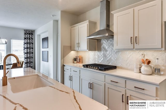 kitchen featuring white cabinetry, stainless steel gas cooktop, wall chimney exhaust hood, and sink