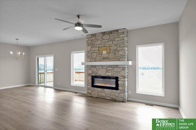 unfurnished living room featuring a fireplace, light wood-type flooring, and ceiling fan with notable chandelier