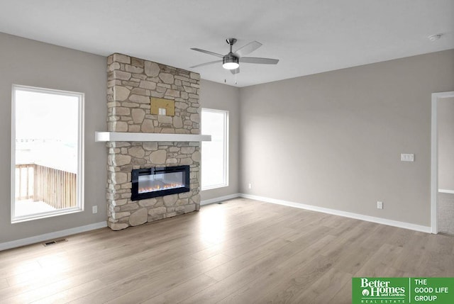 unfurnished living room with light wood-type flooring, a stone fireplace, and ceiling fan