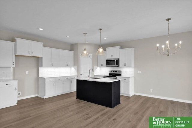 kitchen with stainless steel appliances, a kitchen island with sink, sink, white cabinetry, and hanging light fixtures