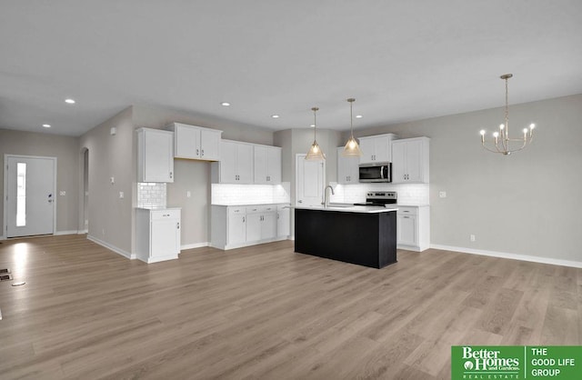 kitchen with white cabinets, pendant lighting, stainless steel appliances, and a center island with sink