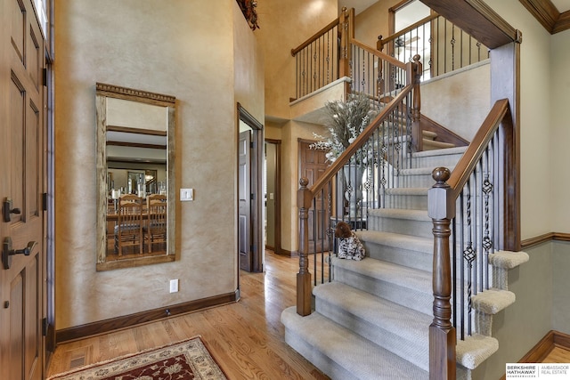 entrance foyer with light hardwood / wood-style flooring, a towering ceiling, and ornamental molding