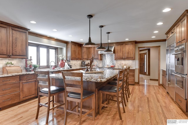 kitchen with a kitchen island, light wood-type flooring, light stone countertops, and crown molding