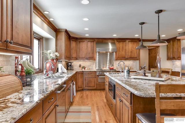 kitchen featuring wall chimney range hood, sink, light stone countertops, light wood-type flooring, and tasteful backsplash