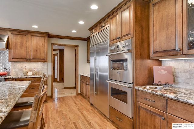 kitchen featuring backsplash, light stone counters, ornamental molding, and appliances with stainless steel finishes