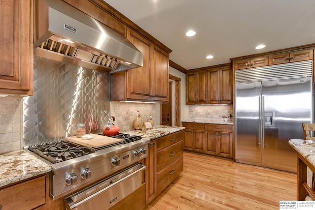 kitchen with tasteful backsplash, light stone counters, stainless steel built in fridge, and wall chimney range hood