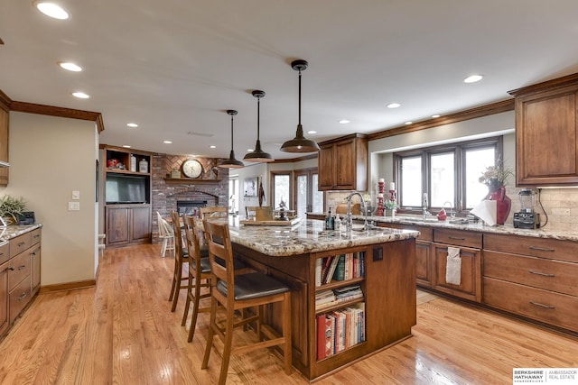 kitchen with a kitchen bar, light wood-type flooring, an island with sink, decorative light fixtures, and light stone counters