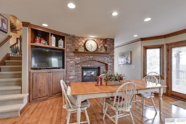 dining area featuring crown molding, light hardwood / wood-style flooring, and a brick fireplace