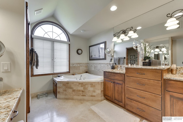 bathroom with tile patterned floors, vanity, a relaxing tiled tub, and vaulted ceiling