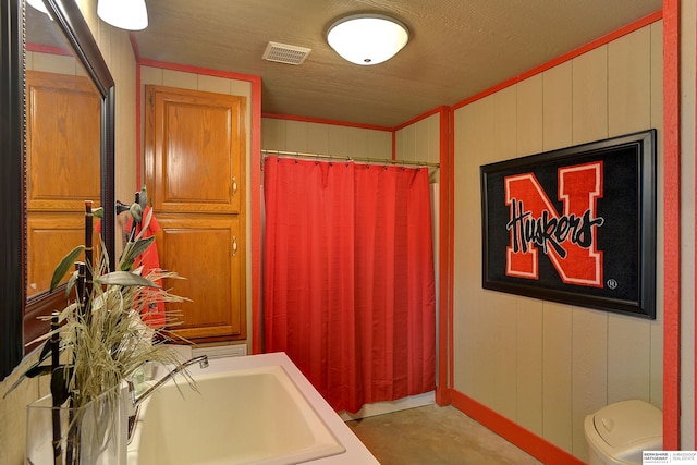 bathroom with wood walls, toilet, and sink