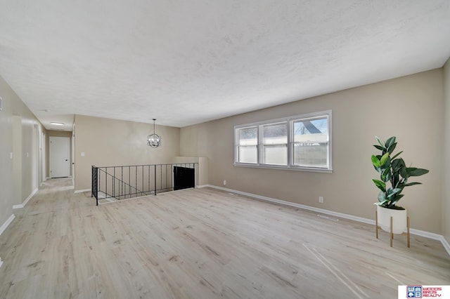 unfurnished living room featuring a chandelier, a textured ceiling, and light wood-type flooring