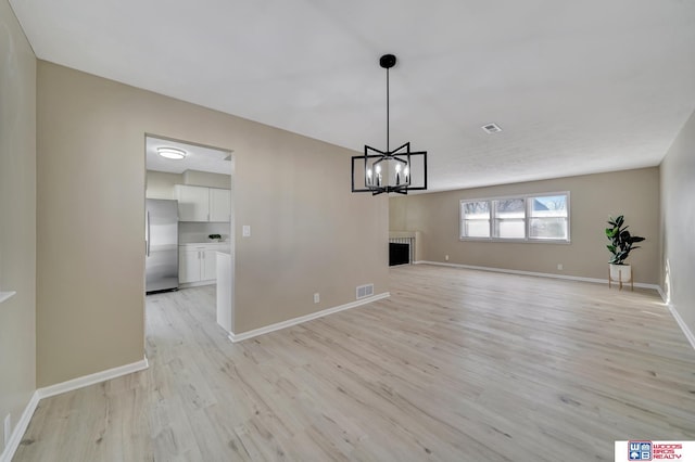 unfurnished dining area featuring an inviting chandelier and light hardwood / wood-style flooring