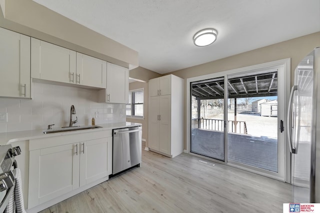 kitchen featuring sink, light hardwood / wood-style flooring, decorative backsplash, white cabinets, and appliances with stainless steel finishes