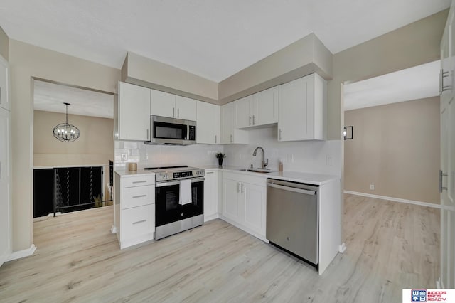 kitchen with appliances with stainless steel finishes, light hardwood / wood-style flooring, white cabinetry, and pendant lighting