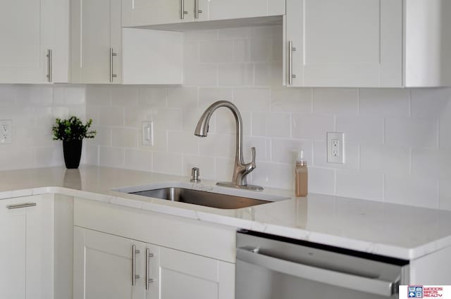 kitchen featuring decorative backsplash, light stone countertops, stainless steel dishwasher, sink, and white cabinetry