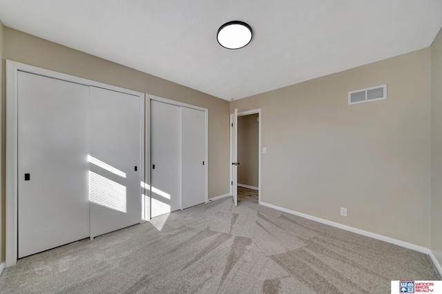 unfurnished bedroom featuring light colored carpet and two closets