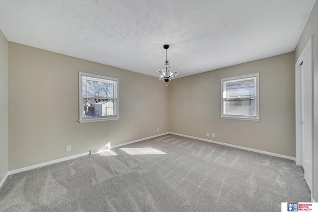 spare room featuring light colored carpet and a notable chandelier