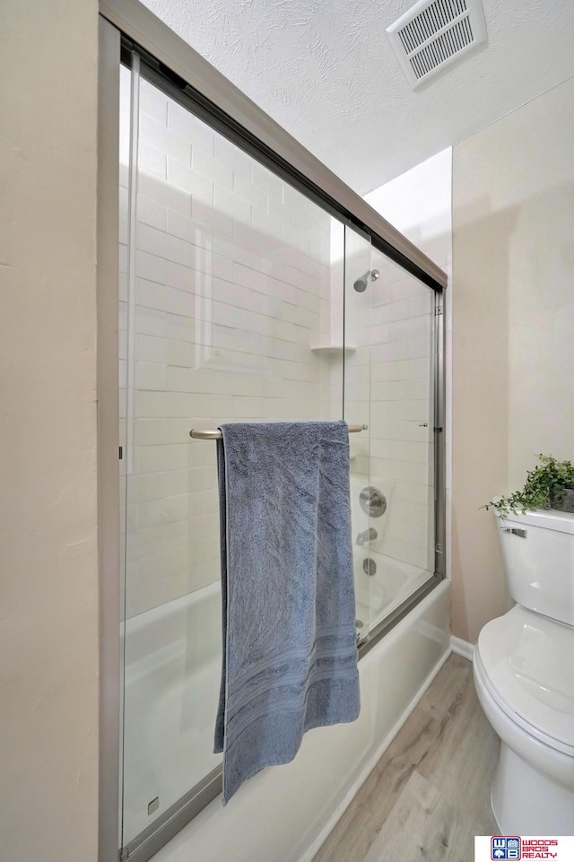 bathroom featuring toilet, wood-type flooring, a textured ceiling, and combined bath / shower with glass door