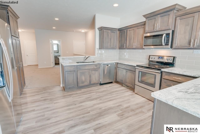 kitchen with sink, stainless steel appliances, tasteful backsplash, light stone counters, and light wood-type flooring