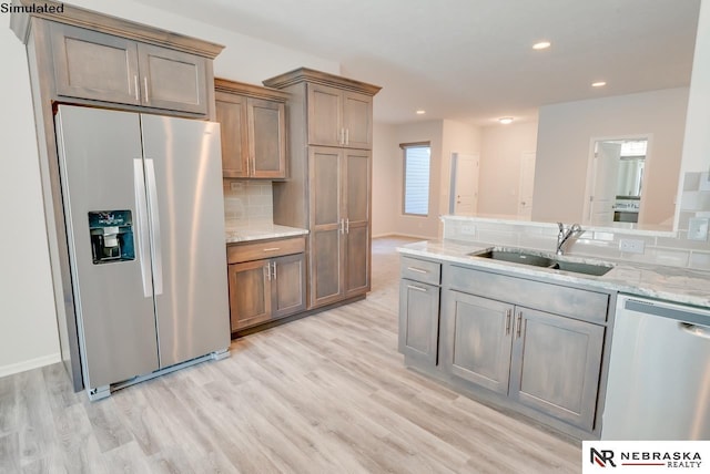 kitchen with light stone countertops, appliances with stainless steel finishes, tasteful backsplash, sink, and light hardwood / wood-style floors