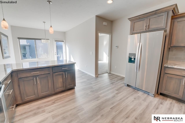 kitchen featuring pendant lighting, backsplash, stainless steel fridge, light wood-type flooring, and light stone counters