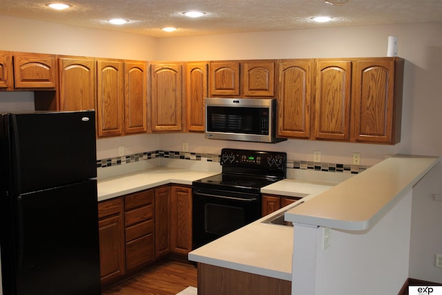 kitchen featuring black appliances, backsplash, hardwood / wood-style flooring, kitchen peninsula, and a textured ceiling