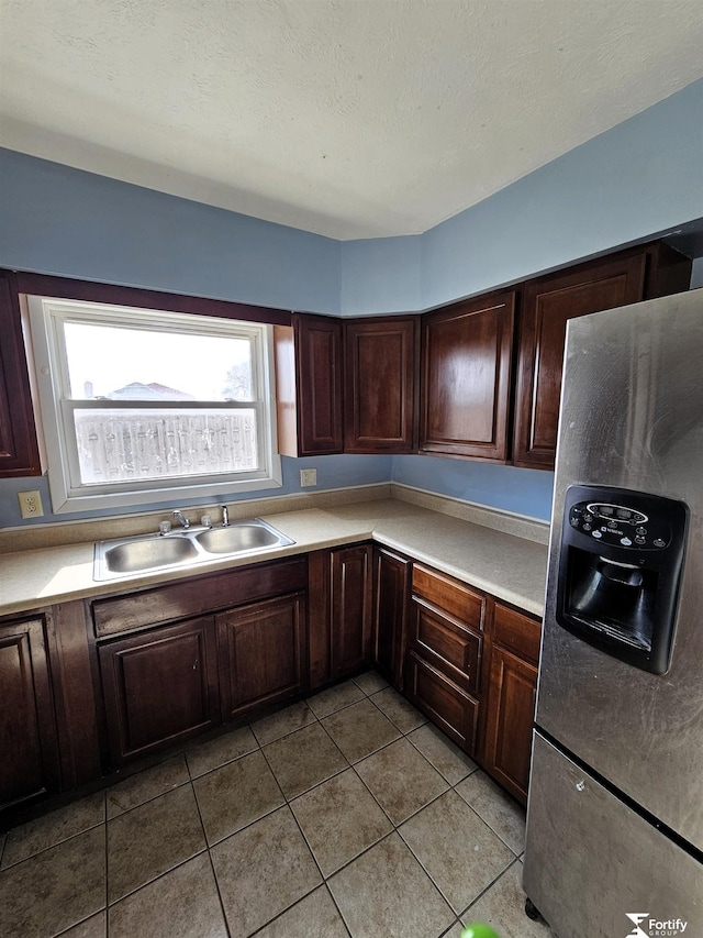 kitchen featuring sink, light tile patterned floors, stainless steel fridge, dark brown cabinetry, and a textured ceiling