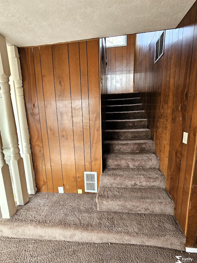 stairs with a textured ceiling and wood walls