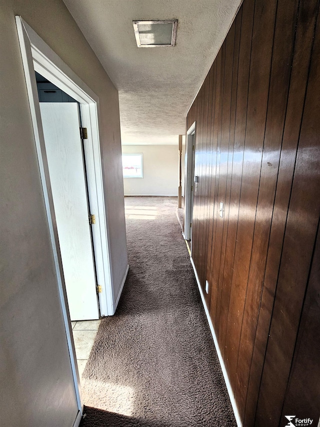 hall featuring carpet flooring, a textured ceiling, and wood walls