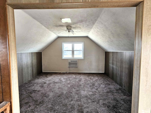 additional living space with wooden walls, a wall mounted AC, a textured ceiling, dark carpet, and vaulted ceiling