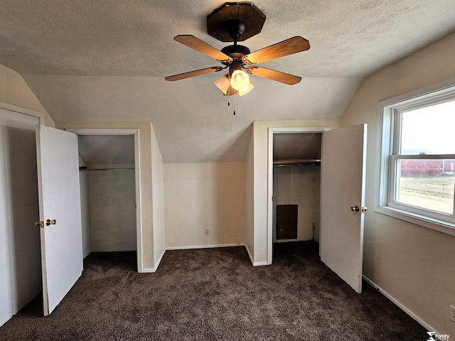 unfurnished bedroom with multiple closets, vaulted ceiling, a textured ceiling, and dark colored carpet