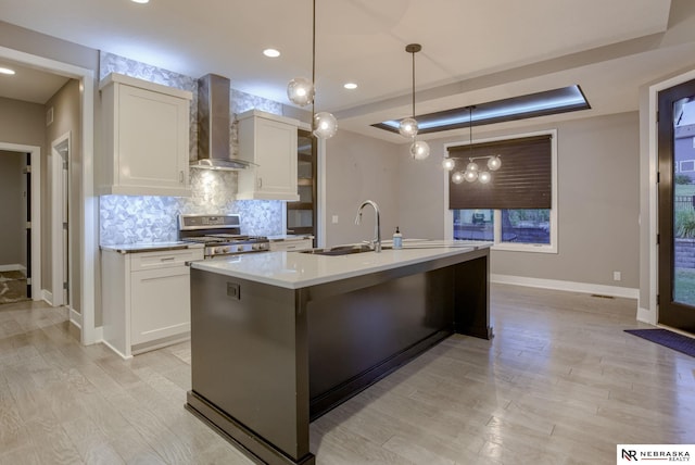 kitchen featuring sink, wall chimney exhaust hood, an island with sink, white cabinets, and range