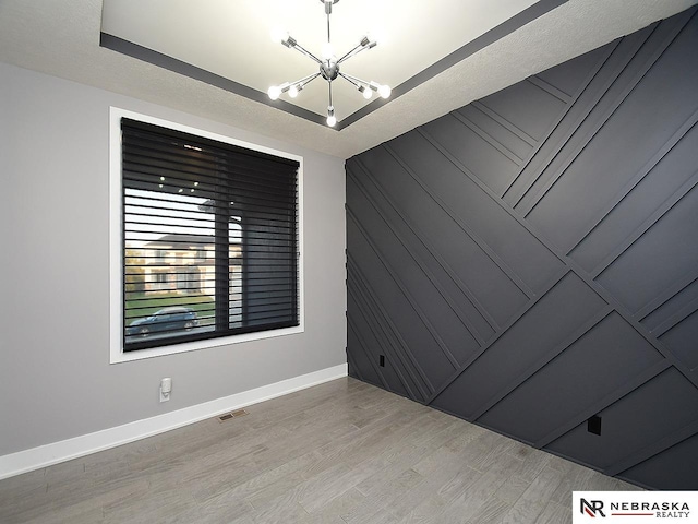 empty room with baseboards, visible vents, wood finished floors, a textured ceiling, and a notable chandelier