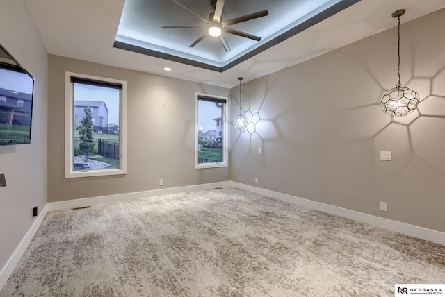 carpeted empty room with a raised ceiling and ceiling fan