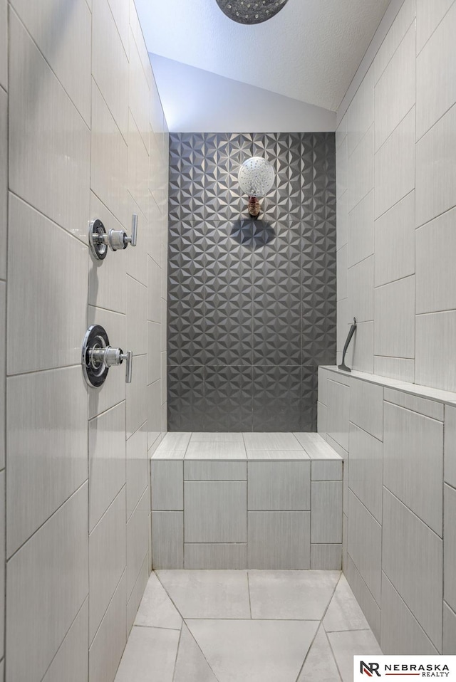 bathroom featuring tile patterned flooring, a tile shower, a textured ceiling, and lofted ceiling