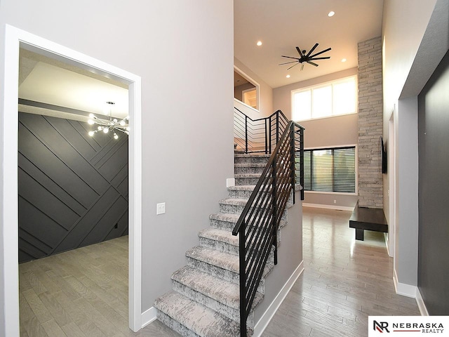 stairway featuring a notable chandelier, recessed lighting, a high ceiling, wood walls, and wood finished floors