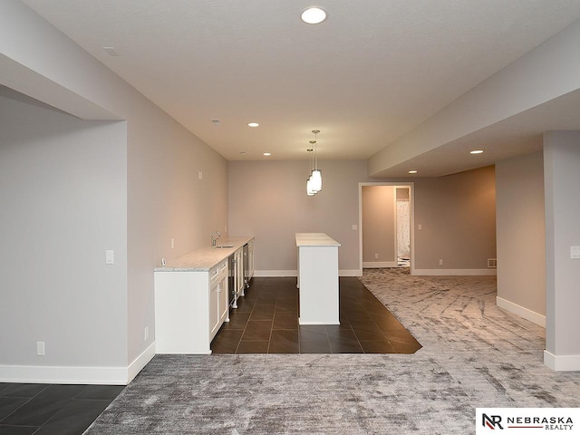 interior space featuring light stone counters, sink, pendant lighting, dark tile patterned flooring, and white cabinets