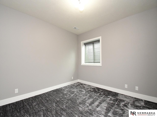 empty room featuring visible vents, baseboards, and dark colored carpet