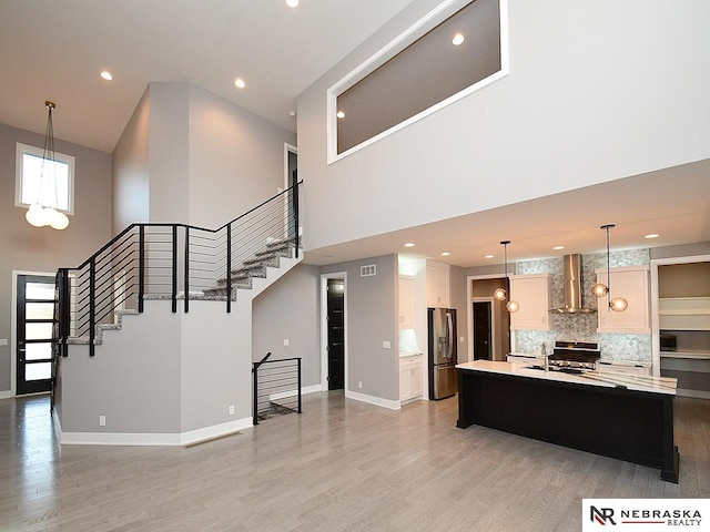 kitchen with wall chimney exhaust hood, stainless steel appliances, a kitchen island with sink, and a high ceiling