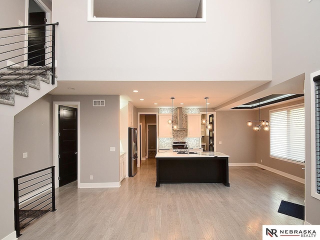 kitchen featuring wall chimney exhaust hood, stainless steel appliances, backsplash, an island with sink, and a chandelier